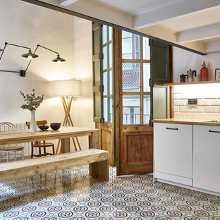This is an example of a mid-sized modern l-shaped eat-in kitchen in Barcelona with a drop-in sink, flat-panel cabinets, white cabinets, wood benchtops, white splashback, ceramic splashback, stainless steel appliances, terra-cotta floors, no island and multi-coloured floor.