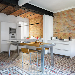 Ejemplo de cocina en U, mediterránea, grande, con armarios con paneles lisos, puertas de armario blancas, electrodomésticos de acero inoxidable, una isla, suelo de baldosas de cerámica, suelo multicolor, salpicadero rojo y salpicadero de ladrillos