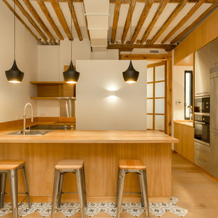 Imagen de cocina en U, mediterránea, de tamaño medio, abierta, con armarios con paneles lisos, puertas de armario de madera oscura, encimera de madera, salpicadero blanco, península, fregadero encastrado, electrodomésticos de acero inoxidable, suelo de madera clara y suelo beige