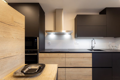 Ejemplo de cocina lineal contemporánea de tamaño medio cerrada con fregadero de un seno, puertas de armario negras, electrodomésticos negros, suelo de baldosas de cerámica y suelo gris