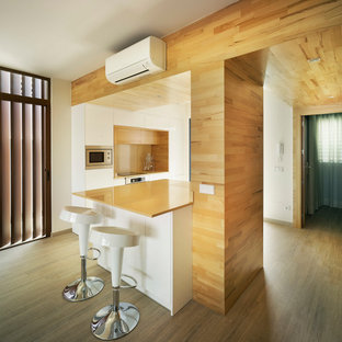 This is an example of a mid-sized contemporary single-wall open plan kitchen in Malaga with flat-panel cabinets, white cabinets, medium hardwood floors, a peninsula and orange benchtop.