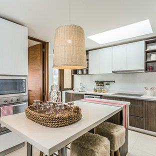 Ejemplo de cocina actual, cerrada, con armarios con paneles lisos, puertas de armario de madera en tonos medios, encimera de cuarzo compacto, salpicadero blanco, electrodomésticos de acero inoxidable, una isla, encimeras blancas y suelo beige