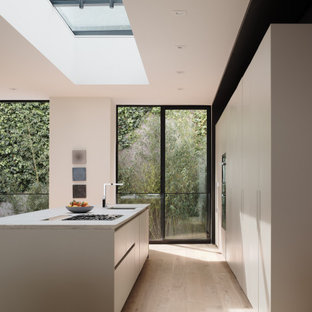 Diseño de cocina de galera, minimalista, con fregadero bajoencimera, armarios con paneles lisos, puertas de armario blancas, electrodomésticos de acero inoxidable, suelo de madera clara, una isla, suelo beige y encimeras blancas
