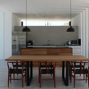 Ejemplo de cocina comedor lineal, moderna, de tamaño medio, con electrodomésticos de acero inoxidable, una isla, suelo gris, encimeras negras, armarios con paneles lisos, puertas de armario blancas, salpicadero verde, fregadero bajoencimera y suelo de baldosas de porcelana