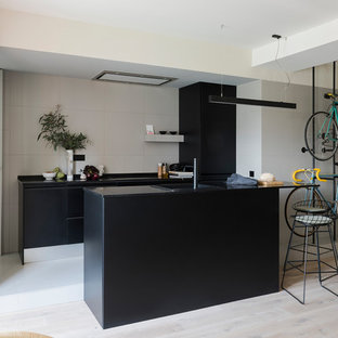 Imagen de cocina lineal, actual, de tamaño medio, abierta, con armarios con paneles lisos, puertas de armario negras, salpicadero beige, una isla y encimeras negras