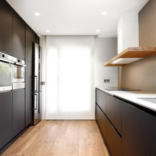 Ejemplo de cocina de galera, minimalista, con fregadero bajoencimera, armarios con paneles lisos, puertas de armario negras, electrodomésticos de acero inoxidable, suelo de madera clara y encimeras blancas
