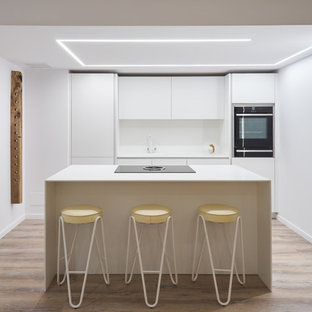 Foto de cocina lineal, actual, con armarios con paneles lisos, puertas de armario blancas, salpicadero blanco, electrodomésticos negros, una isla y encimeras blancas