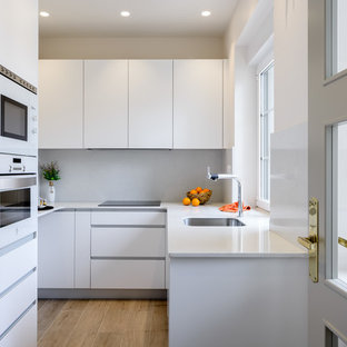 Imagen de cocina en U, actual, cerrada, con armarios con paneles lisos, puertas de armario blancas, salpicadero blanco, encimeras blancas, encimera de cuarzo compacto, electrodomésticos blancos, fregadero bajoencimera, suelo de madera clara y suelo beige