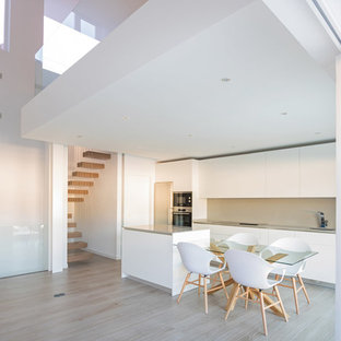 Ejemplo de cocina comedor lineal, minimalista, con fregadero bajoencimera, armarios con paneles lisos, puertas de armario blancas, salpicadero beige, electrodomésticos de acero inoxidable, suelo de madera clara, península, suelo beige y encimeras beige