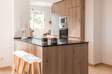 Cette image montre une cuisine ouverte parallèle nordique en bois brun avec un évier encastré, un plan de travail en quartz modifié, un électroménager en acier inoxydable, un sol en marbre, îlot, un sol beige et plan de travail noir.