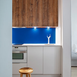 Diseño de cocina nórdica, pequeña, con fregadero bajoencimera, puertas de armario de madera oscura, salpicadero azul, electrodomésticos blancos, suelo de madera clara y encimeras blancas