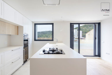 Ejemplo de cocina comedor actual grande con electrodomésticos negros, suelo de madera clara, península y encimeras blancas