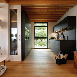 Ejemplo de cocina de galera, contemporánea, abierta, sin isla, con fregadero bajoencimera, armarios con paneles lisos, puertas de armario negras, encimera de granito, salpicadero negro, electrodomésticos negros, suelo de madera en tonos medios y suelo marrón
