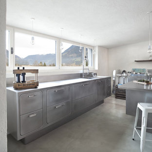 Idee per una grande cucina industriale con lavello integrato, ante lisce, ante in acciaio inossidabile, top in acciaio inossidabile, pavimento in cemento e isola