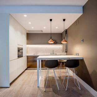 Modelo de cocina en L, actual, abierta, sin isla, con puertas de armario blancas, salpicadero blanco, encimeras blancas, fregadero de un seno, armarios con paneles lisos, electrodomésticos con paneles, suelo de madera clara y suelo beige
