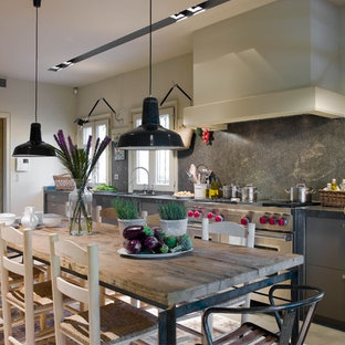 Modelo de cocina comedor lineal, de estilo de casa de campo, grande, con armarios con paneles lisos, puertas de armario grises, salpicadero verde, encimeras grises, salpicadero de losas de piedra, electrodomésticos de acero inoxidable, suelo de cemento y suelo gris