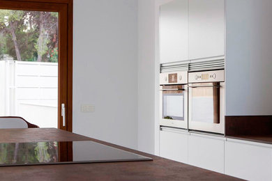Modelo de cocina lineal moderna grande abierta con fregadero de un seno, armarios con paneles lisos, puertas de armario blancas y una isla