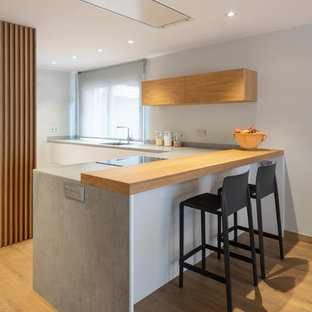 Modelo de cocina en L, minimalista, con suelo de madera en tonos medios, península, encimeras grises, armarios con paneles lisos, puertas de armario blancas y suelo marrón
