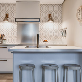 Foto de cocina de galera, clásica renovada, con fregadero encastrado, armarios con paneles lisos, puertas de armario blancas, salpicadero blanco, electrodomésticos de acero inoxidable, suelo de madera en tonos medios, suelo marrón y encimeras blancas