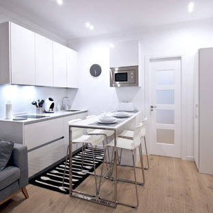 Ejemplo de cocina escandinava, pequeña, abierta, con armarios con paneles lisos, puertas de armario blancas, salpicadero blanco, electrodomésticos de acero inoxidable, península, encimeras blancas, fregadero bajoencimera y suelo de madera clara