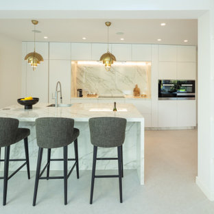 Imagen de cocina de galera, contemporánea, con fregadero bajoencimera, armarios con paneles lisos, puertas de armario blancas, salpicadero blanco, salpicadero de losas de piedra, electrodomésticos de acero inoxidable, una isla, suelo gris y encimeras blancas