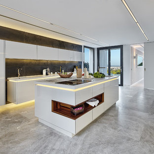 Diseño de cocina de galera, contemporánea, grande, con fregadero integrado, armarios con paneles lisos, puertas de armario blancas, encimera de acrílico, salpicadero negro, salpicadero de pizarra, electrodomésticos de acero inoxidable, suelo de piedra caliza, una isla, encimeras blancas y suelo gris