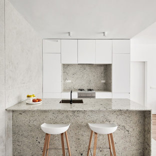Modelo de cocina moderna con fregadero bajoencimera, armarios con paneles lisos, puertas de armario blancas, salpicadero verde, electrodomésticos de acero inoxidable, península y suelo gris