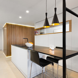 Diseño de cocina contemporánea, de tamaño medio, con armarios con paneles lisos, puertas de armario blancas, encimera de cuarzo compacto, suelo de cemento, una isla, encimeras negras y suelo beige