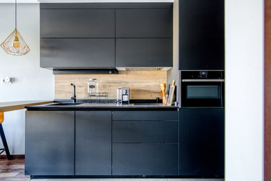 Diseño de cocina lineal minimalista de tamaño medio con fregadero integrado, salpicadero negro, electrodomésticos negros y encimeras negras