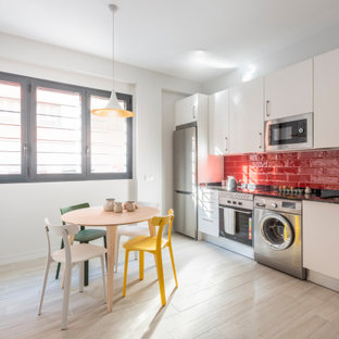 Diseño de cocina comedor lineal, contemporánea, de tamaño medio, sin isla, con fregadero bajoencimera, armarios con paneles lisos, puertas de armario blancas, salpicadero rojo, salpicadero de azulejos tipo metro, electrodomésticos de acero inoxidable, suelo beige y encimeras negras