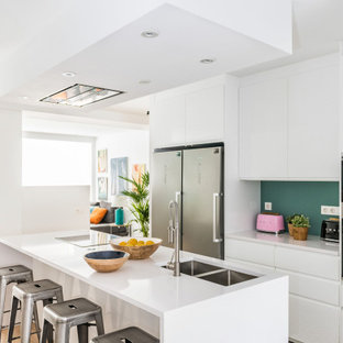 Imagen de cocina de galera, actual, con armarios con paneles lisos, puertas de armario blancas, electrodomésticos de acero inoxidable, suelo de madera clara, una isla, suelo beige, encimeras blancas, fregadero bajoencimera y salpicadero gris
