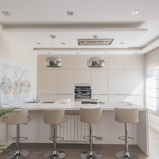 Imagen de cocina actual con fregadero de doble seno, armarios con paneles lisos, puertas de armario beige, electrodomésticos de acero inoxidable, suelo de madera clara, península, suelo beige y encimeras blancas
