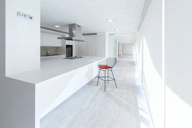 Photo of a large modern u-shaped kitchen in Alicante-Costa Blanca with a single-bowl sink, flat-panel cabinets, white cabinets, engineered stone countertops, grey splashback, stone slab splashback, white appliances, porcelain flooring, an island, white floors and white worktops.