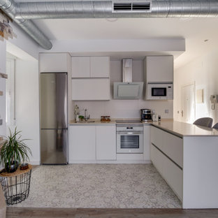 Imagen de cocina en L, contemporánea, con fregadero bajoencimera, armarios con paneles lisos, puertas de armario blancas, electrodomésticos de acero inoxidable, península y suelo blanco