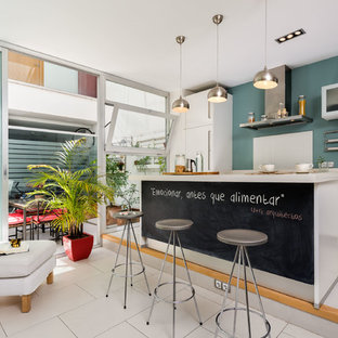 Modelo de cocina lineal, contemporánea, de tamaño medio, abierta, con armarios con paneles lisos, puertas de armario blancas, salpicadero azul, una isla y suelo blanco