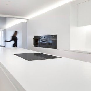 Modelo de cocina de galera, moderna, extra grande, abierta, con armarios con paneles lisos, puertas de armario blancas, encimera de cuarzo compacto, salpicadero blanco, suelo de baldosas de cerámica, una isla, suelo beige, encimeras blancas, fregadero bajoencimera y electrodomésticos negros