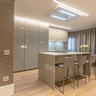 Ejemplo de cocina de galera, actual, con puertas de armario beige, una isla, suelo de madera en tonos medios, fregadero bajoencimera, armarios con paneles lisos, salpicadero verde, electrodomésticos con paneles, suelo beige y encimeras beige
