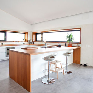 Modelo de cocina comedor en U, escandinava, con armarios con paneles lisos, puertas de armario blancas, encimera de madera, electrodomésticos de acero inoxidable, suelo de cemento, península, suelo gris y encimeras marrones