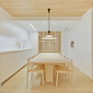 Foto de cocina comedor actual, de tamaño medio, sin isla, con armarios con paneles lisos, puertas de armario blancas, salpicadero blanco, electrodomésticos blancos, suelo de madera clara, suelo beige, encimeras blancas y salpicadero de losas de piedra
