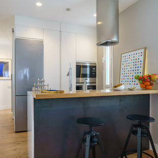 Diseño de cocina en U, actual, pequeña, con armarios con paneles lisos, puertas de armario blancas, encimera de madera, electrodomésticos con paneles, suelo de madera clara, península, suelo beige y encimeras beige