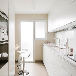 Modelo de cocina de galera, moderna, de tamaño medio, con electrodomésticos de acero inoxidable, salpicadero blanco, fregadero bajoencimera, armarios con paneles lisos, puertas de armario blancas, península, suelo beige y encimeras blancas