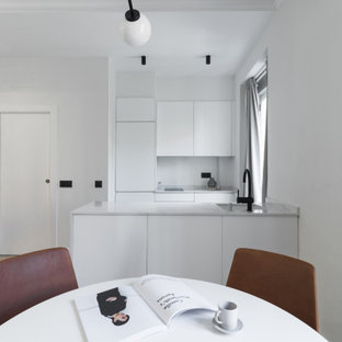 Ejemplo de cocina comedor de galera, contemporánea, pequeña, con fregadero bajoencimera, armarios con paneles lisos, puertas de armario blancas, electrodomésticos con paneles, suelo de madera clara, península, suelo beige y encimeras blancas