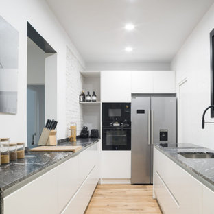 Ejemplo de cocina en U, actual, sin isla, con fregadero bajoencimera, armarios con paneles lisos, puertas de armario blancas, electrodomésticos de acero inoxidable, suelo de madera clara, suelo beige y encimeras negras