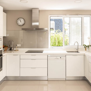 Foto de cocina en U, contemporánea, de tamaño medio, cerrada, sin isla, con fregadero bajoencimera, armarios con paneles lisos, puertas de armario blancas, salpicadero beige, salpicadero de vidrio templado, electrodomésticos de acero inoxidable, suelo beige y encimeras blancas