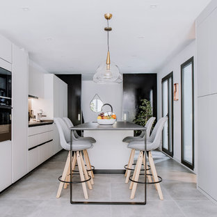 Foto de cocina de galera, actual, grande, con fregadero de doble seno, armarios con paneles lisos, encimera de cuarzo compacto, electrodomésticos con paneles, suelo de baldosas de porcelana, una isla, suelo gris, encimeras negras y puertas de armario blancas