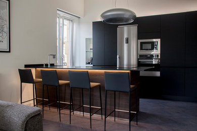 Foto de cocinas en U minimalista de tamaño medio abierto con electrodomésticos de acero inoxidable, península y encimeras negras