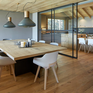 Modelo de comedor de estilo de casa de campo, grande, abierto, con suelo de madera clara, paredes grises y suelo marrón