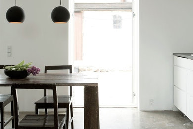 Foto di una piccola sala da pranzo aperta verso la cucina contemporanea con pareti bianche, pavimento in cemento e nessun camino