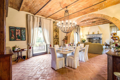 Diseño de comedor mediterráneo abierto con paredes beige, suelo de baldosas de terracota, todas las chimeneas, marco de chimenea de yeso, suelo naranja y cortinas