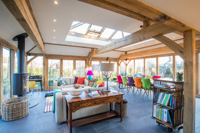 This is an example of a large eclectic conservatory in Cambridgeshire with a wood burning stove, a skylight, a metal fireplace surround and grey floors.